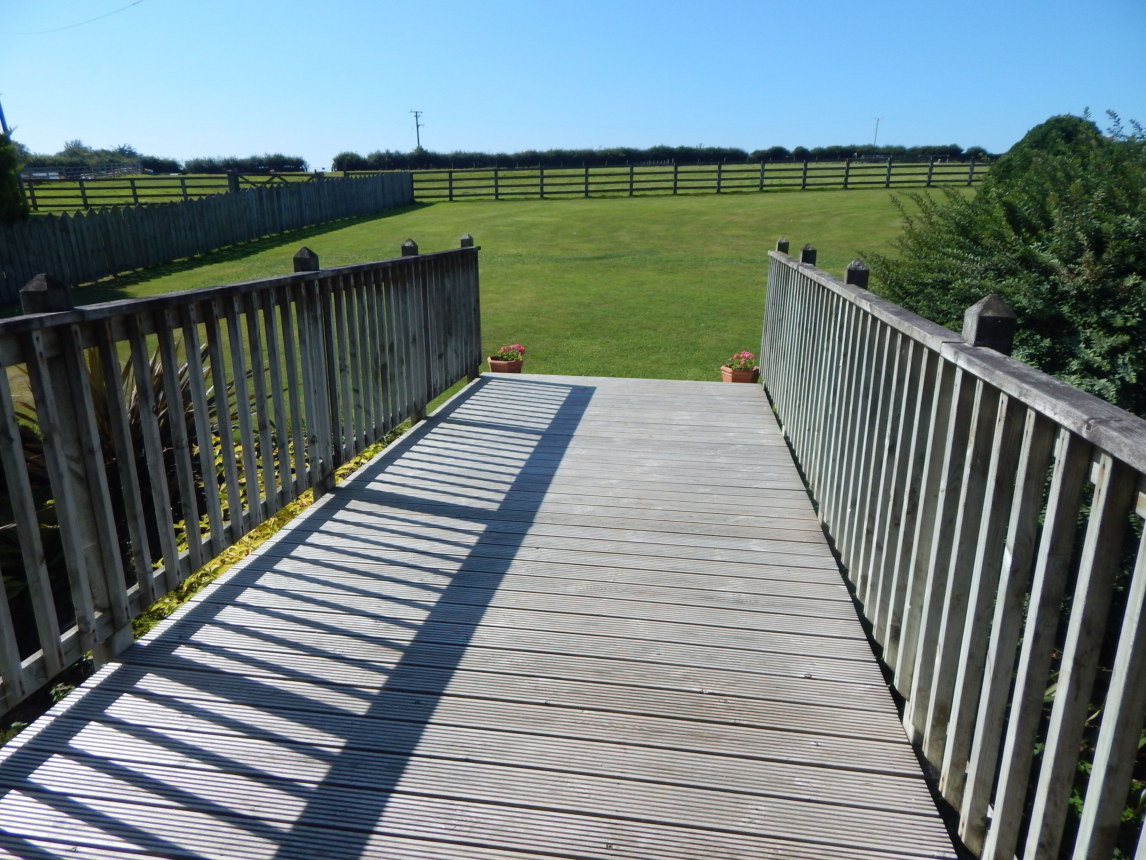 A wooden deck leading to a grassy field with a wooden fence.