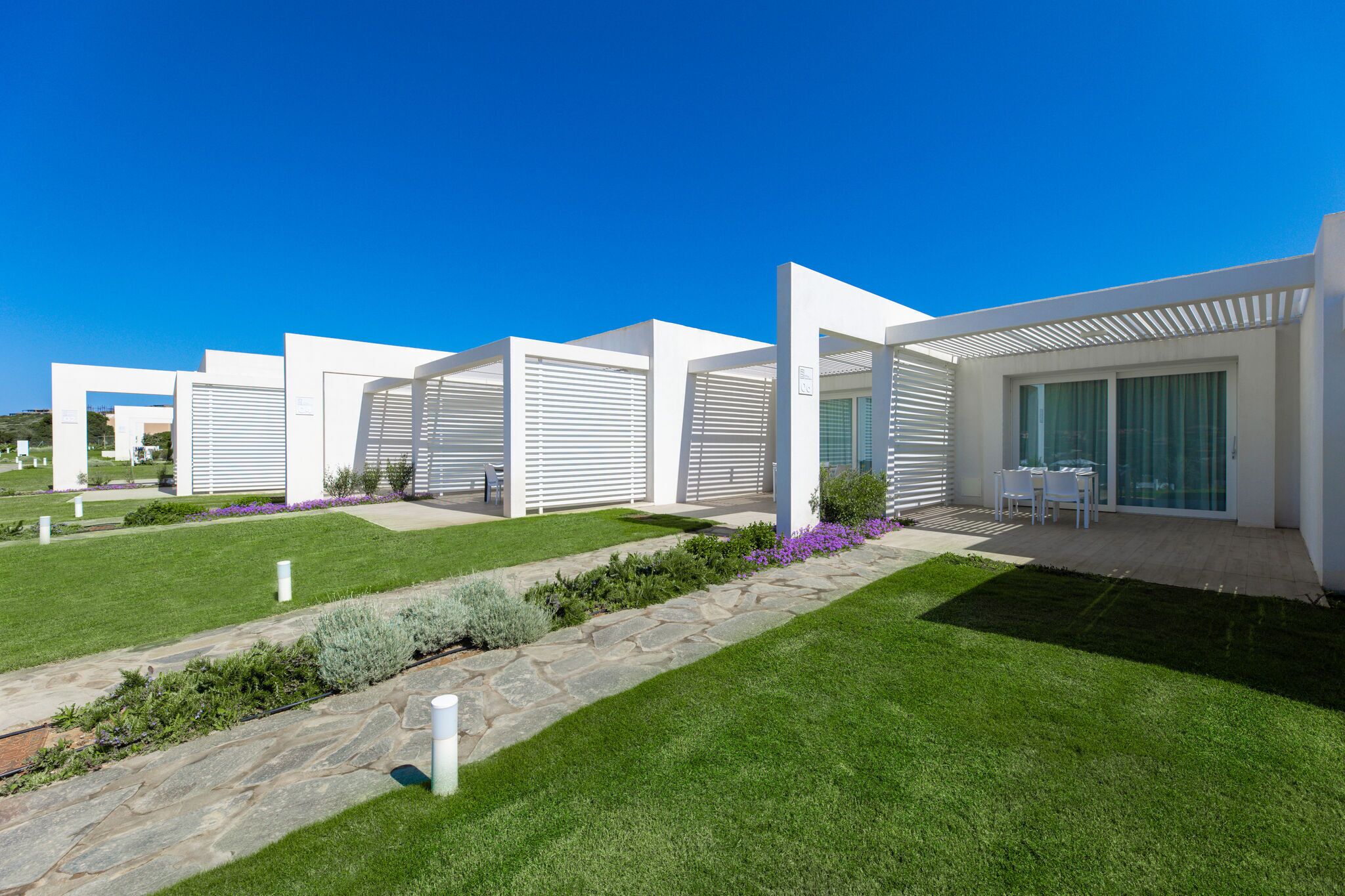 A modern building with white exterior walls, large windows, and a well-maintained lawn.