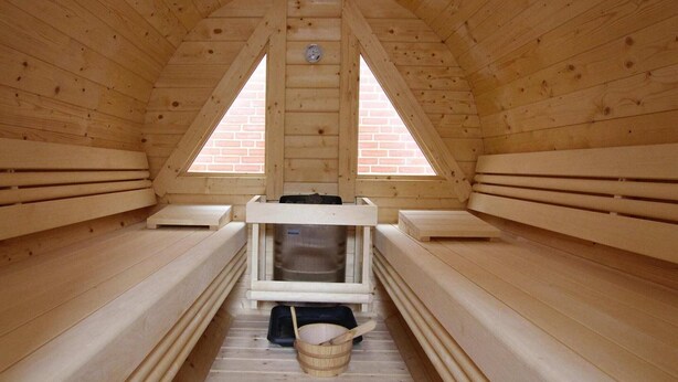 A sauna with wooden benches and a central bench with a bucket and a towel. - Appartement in Westerland auf Sylt (Westerland)