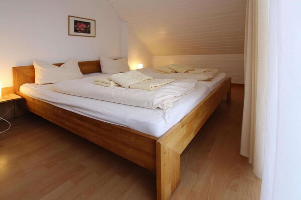 A large, wooden-framed bed with white linens and towels neatly arranged on top.