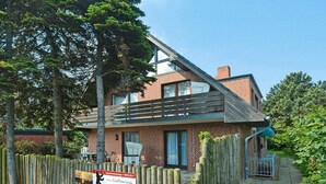 A two-story brick building with a sloped roof, a covered outdoor seating area, and a sign indicating a bus stop for Katharina. - Appartement in Westerland auf Sylt (Westerland)