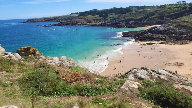 A coastal landscape with a sandy beach, rocky outcrops, and a clear blue sea.