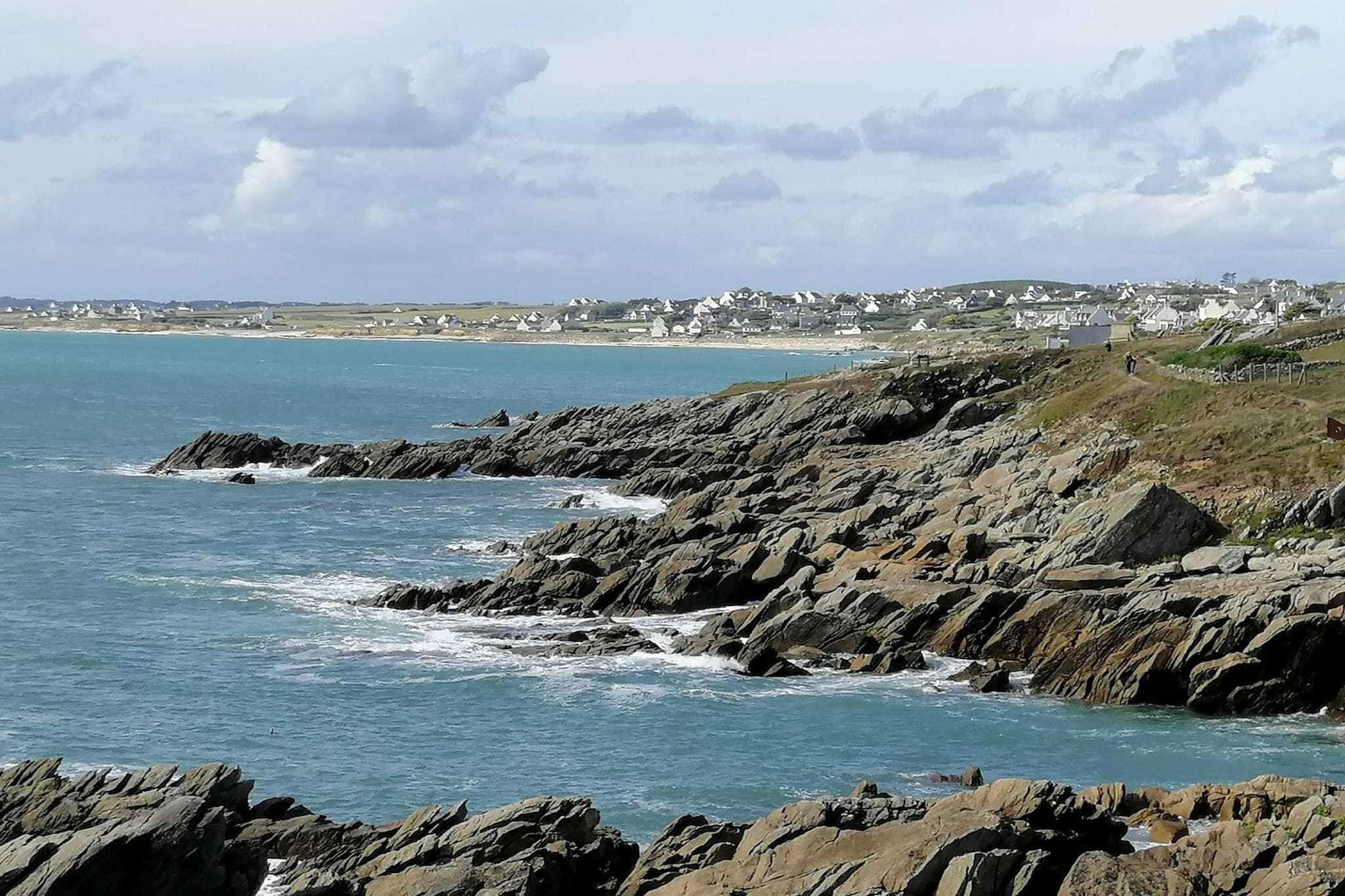 A coastal landscape with rocky terrain and a view of a small town in the distance.