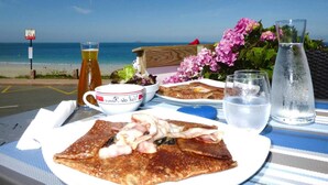 A table set with breakfast items, including a plate of food, a glass of juice, and a pitcher of water, with a beach view in the background.