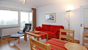 Un salon moderne avec un canapé rouge, des chaises en bois, une table basse et un lampadaire.