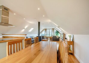 A spacious loft with a wooden dining table, a built-in stove, and a large window providing natural light.