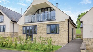 Une maison moderne à deux étages, dotée d’un balcon, d’une façade en pierre et d’une allée pavée.