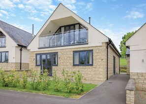 Une maison moderne à deux étages, dotée d’un balcon, d’une façade en pierre et d’une allée pavée.