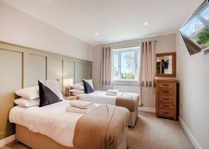 A bedroom with two beds, a dresser, a mirror, and a window with curtains.
