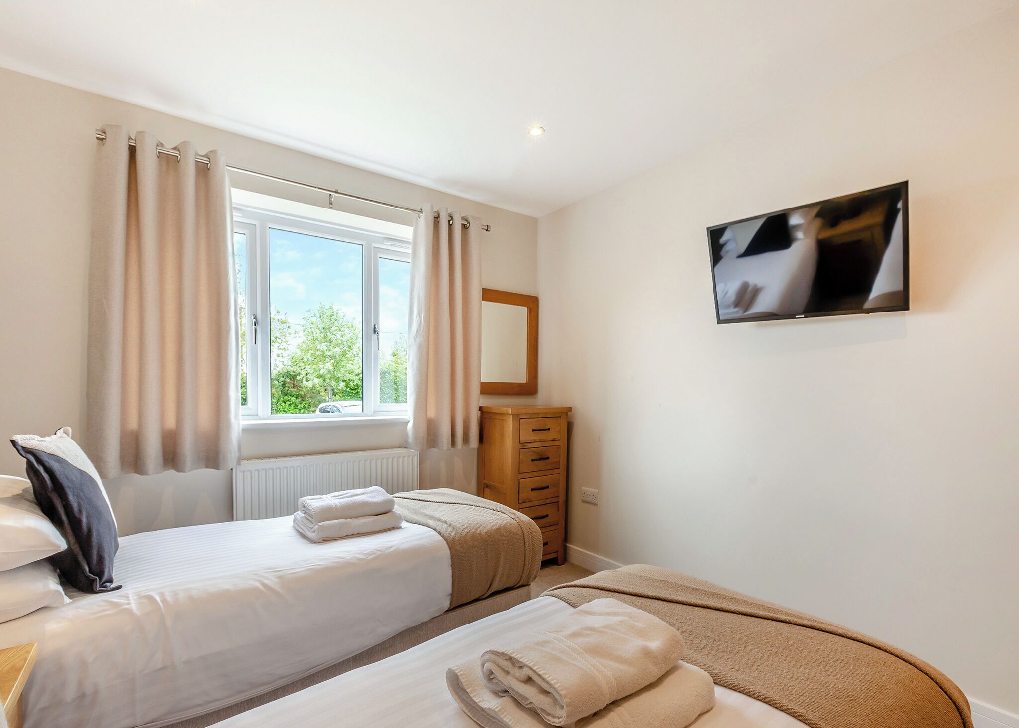A bedroom with two beds, a dresser, a mirror, and a TV.