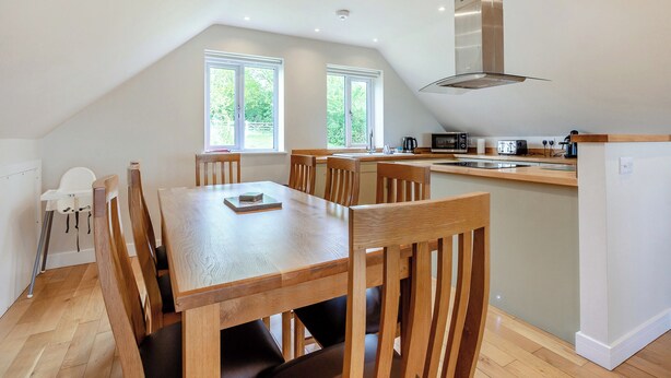 Una cocina moderna con una isla central, mesa de comedor de madera y sillas, con ventanas grandes que permiten la entrada de luz natural.