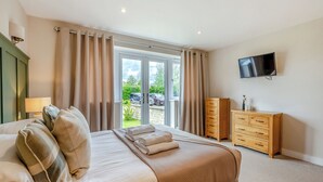 Une chambre d’hôtel équipée d’un lit, d’une commode, d’une télévision et d’une porte-fenêtre coulissante donnant sur l’extérieur.