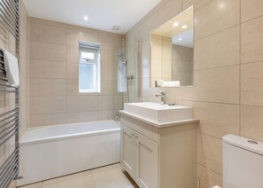 A modern bathroom with a bathtub, a sink, a mirror, and a window.