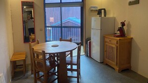Een kleine keuken met een eettafel, stoelen, een koelkast en een houten kast.