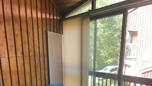 Een kamer met een blauwe bank, een kleine tafel en een raam met uitzicht op een balkon en bomen.