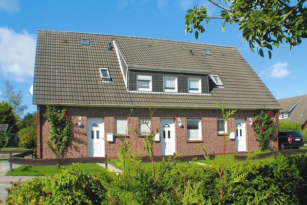 Une maison à deux étages, construite en briques, avec un toit en pente, de nombreuses fenêtres et un petit garage attenant.