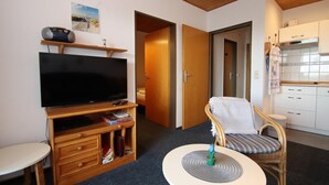 A room with a TV, wooden furniture, a dining table, and a kitchen area. - Ferienwohnung Tiefblick, Dornumersiel (Dornumersiel)