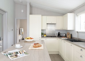 A modern kitchen with white cabinetry, a central island with a bowl of fruit and bread, a stove, and a sink.