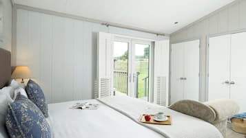 A bedroom with a bed, a nightstand, a lamp, a window with a view of the outdoors, and a door.