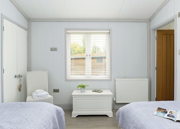 A bedroom with two beds, a window with blinds, a radiator, and a wooden door.