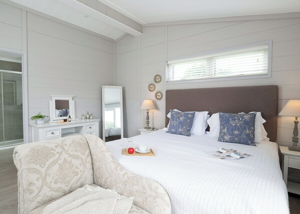 Une chambre à coucher avec un grand lit, des tables de chevet, une commode, un miroir et une fenêtre avec des stores.