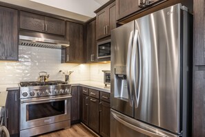 Una cocina moderna con armarios de madera oscura, electrodomésticos de acero inoxidable, incluyendo un refrigerador, horno y estufa, y un salpicadero de azulejos.