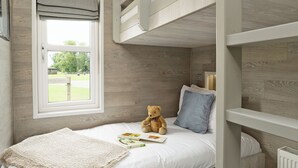 Een slaapkamer met stapelbed, raam, een teddybeer en een deken.