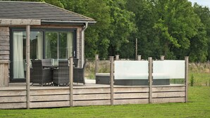 Een houten vakantiehuis met een glazen deur, rieten meubels en een terras met gras.