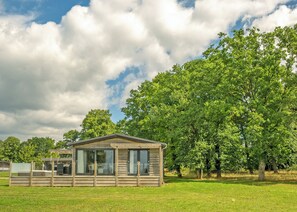 Eine Holzhütte mit Glastür, umgeben von einer Wiese und großen Bäumen.