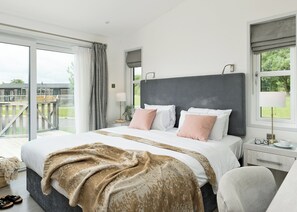 Ein Schlafzimmer mit einem großen Bett, einem Nachttisch, einer Lampe und Blick ins Freie.