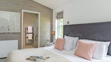 A bedroom with a large bed, a bedside table, a nightstand, a window, and a door leading to a bathroom.