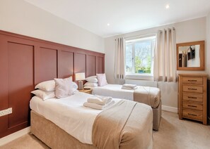 A bedroom with two beds, a wooden dresser, a window with curtains, and a mirror.