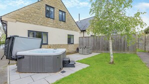 Ein Haus mit einer Steinaußenwand, einem Whirlpool, einem Baum und einem Holzzaun.
