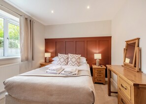 Un dormitorio con una cama grande, dos mesitas de noche, un velador, un espejo y una ventana con cortinas.