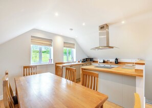A modern kitchen with a wooden table and chairs, a built-in oven, and a window with a view of greenery.