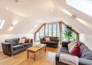 Um amplo loft com duas sofás, uma mesa de centro de madeira e grandes janelas com vista para o exterior.