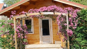 Una cabaña de madera con un porche cubierto de enredaderas con flores rosadas.