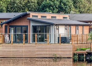 A modern houseboat with a wooden deck, large windows, and a covered outdoor area.