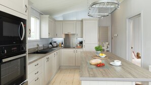 A modern kitchen with white cabinetry, a built-in oven, a microwave, and a hanging light fixture.
