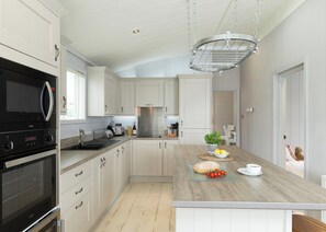 A modern kitchen with white cabinetry, a built-in oven, a microwave, and a hanging light fixture. - 2 bedroom accommodation in Honiton (Honiton)