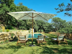 A poolside area with a large umbrella, two wooden lounge chairs, and a stone wall. - Magnificent Mas Provençal in the southern Luberon (Lauris)