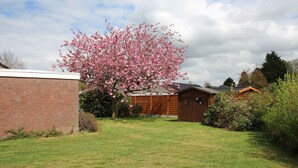 A brick building with a wooden shed, a cherry blossom tree, and a grassy yard. - Bungalow in Berumbur nahe Norddeich Strand (Berumbur)