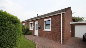 A brick house with a white door, a garage, and a paved driveway. - Bungalow in Berumbur nahe Norddeich Strand (Berumbur)