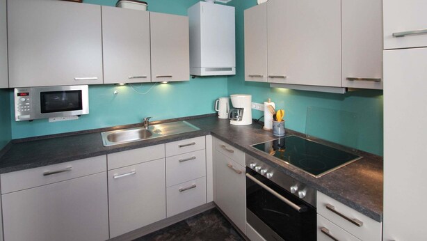 A compact kitchen with white cabinets, a microwave, a coffee maker, and a stove. - Bungalow in Berumbur nahe Norddeich Strand (Berumbur)