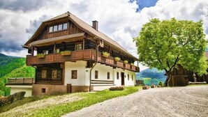 A traditional wooden chalet with a balcony, set against a mountainous backdrop.