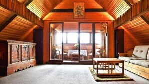 A cozy attic room with wooden beams, a large sliding glass door leading to a dining area, and a sofa.