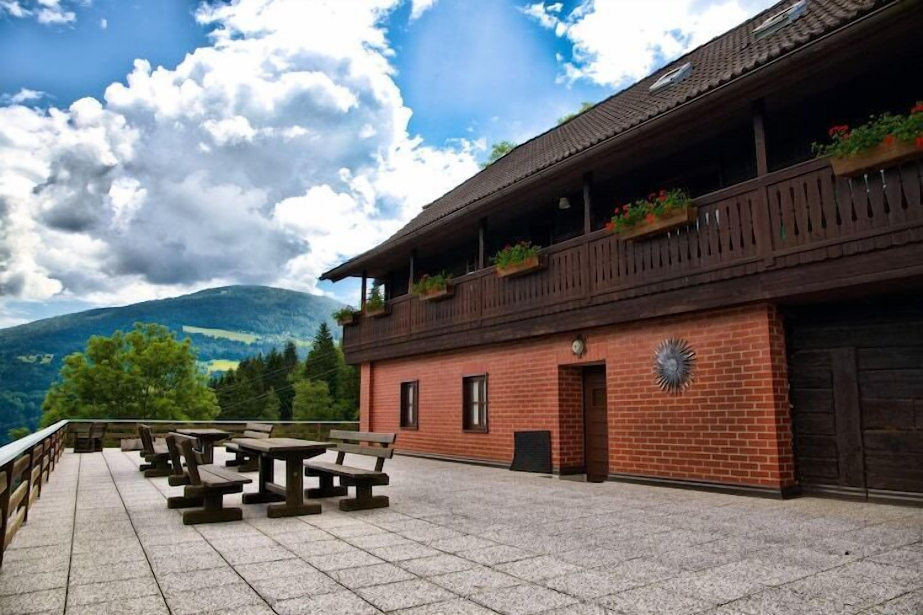 A rustic building with a balcony, outdoor seating, and a mountainous backdrop.