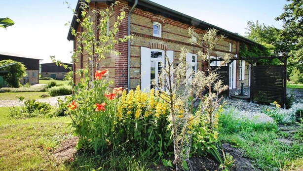 Ein Backsteinhaus mit weißen Fensterläden, umgeben von einem Garten mit verschiedenen Pflanzen und Blumen.