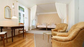 Ein Zimmer mit Holzboden, einem Bett mit weißen Vorhängen, einem Sessel, einem Tisch und einem Spiegel.