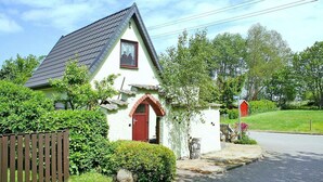 Et hyggeligt hus med skråt tag, rødlakeret dør og en lille veranda.